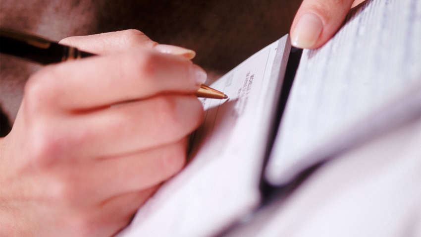 A close-up of a hand holding a pen and filling out paperwork