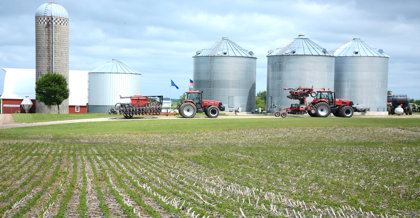 farmstead with tractors, grain bins, silo and cornfield