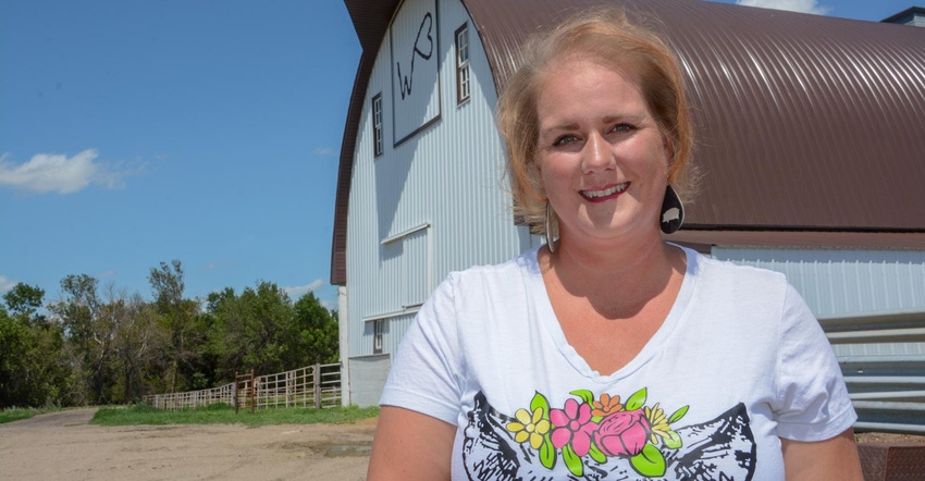 North Dakota farmer, Heather Lang, stands in front of a white and brown barn smiling for a photo