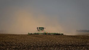 A tractor at work in the field in the middle of a dust cloud