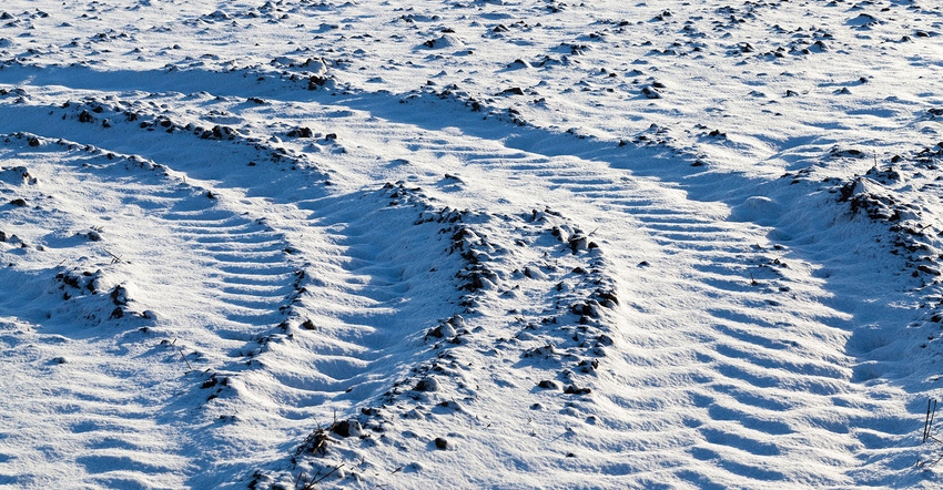a large number of tractor tracks and other equipment on the plowed field soil, covered with snow in winter, closeup