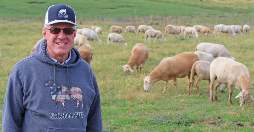 Missouri farmer Lynn Fahrmeier standing with sheep behind him grazing in pasture