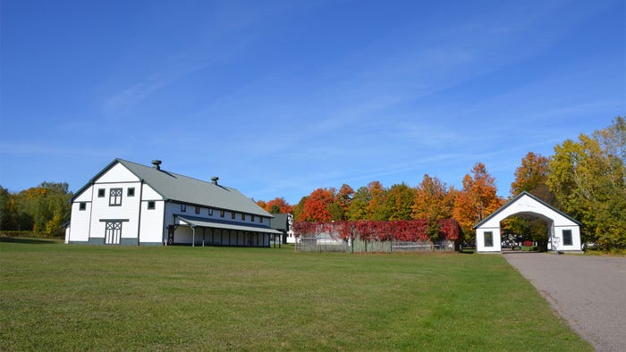 A large and white barn and entrance arcade with colorful trees in the background