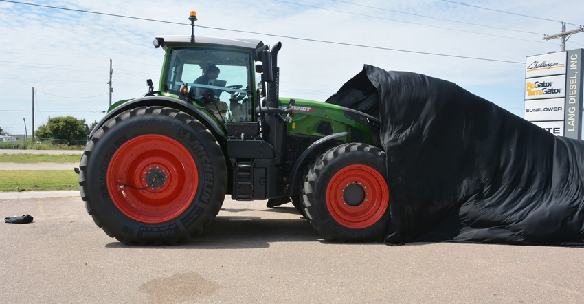 Workers pull the tarp covering the new Fendt 900 series tractor making a visit to the Lang Diesel dealership in Garden City i