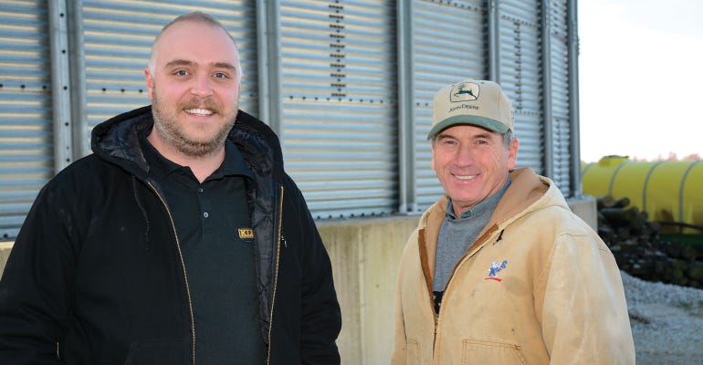 Two guys in front of a grain bin looking at the camera.