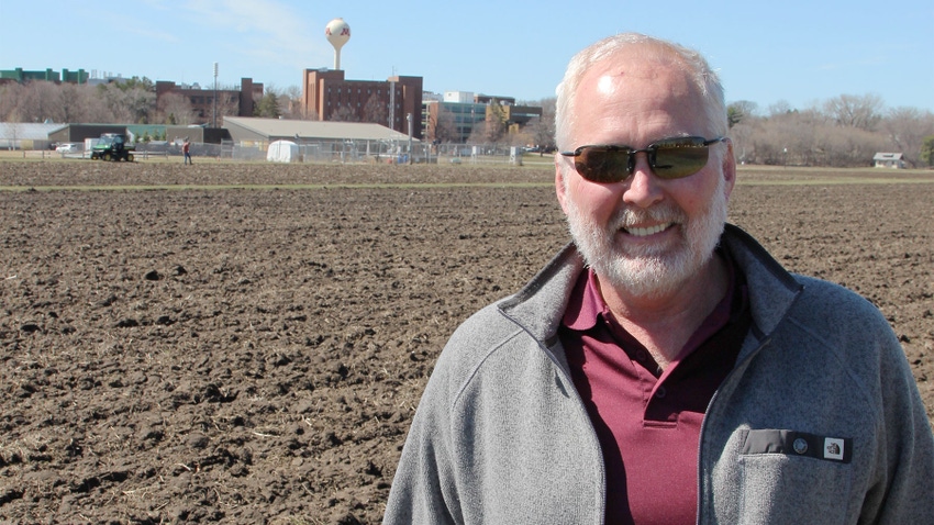 Man in plowed field with University of Minnesota water tower behind him