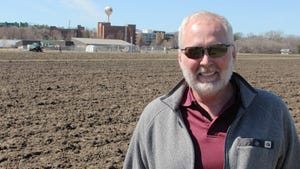 Man in plowed field with University of Minnesota water tower behind him