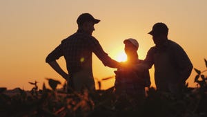 Three people standing in a farm field at sunset shaking hands.