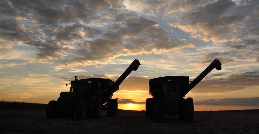 silhouettes of 2 combines side by side at sunset