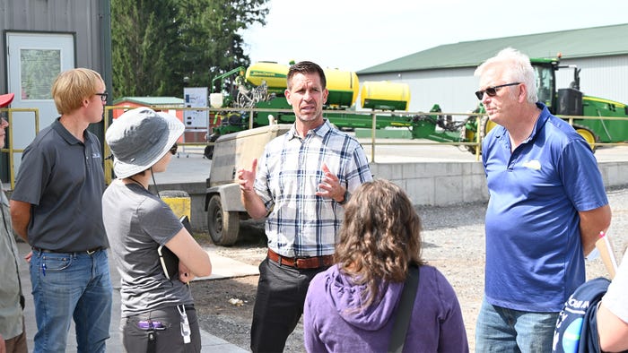 Todd Dumond speaking to a group of people near farming equipment