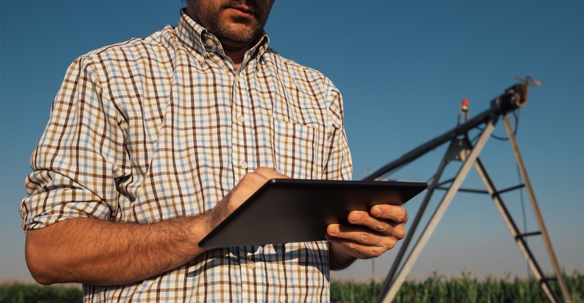 Serious concerned farmer using tablet computer in cornfield with irrigation system out of operation during warm summer day