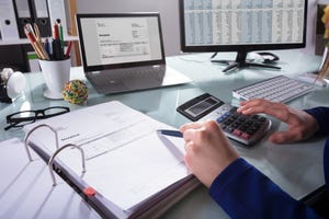 Close-up Of A Businessperson's Hand Calculating Invoice At Workplace