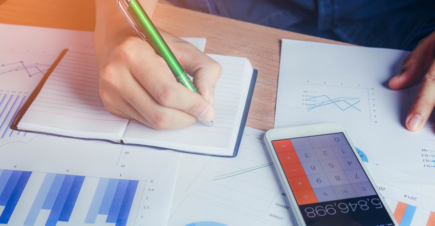 hand writing in notebook with financial papers and calculator on table