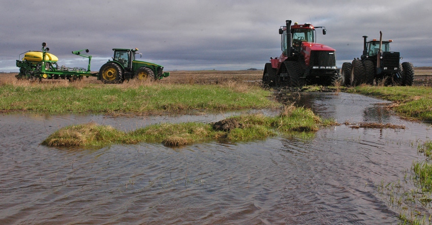 Tractors and planters sit idle at the edge of field that has standing water