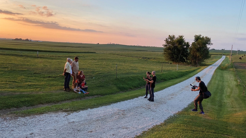 A camera crew capturing video and photo of a family on a rural road at sunset