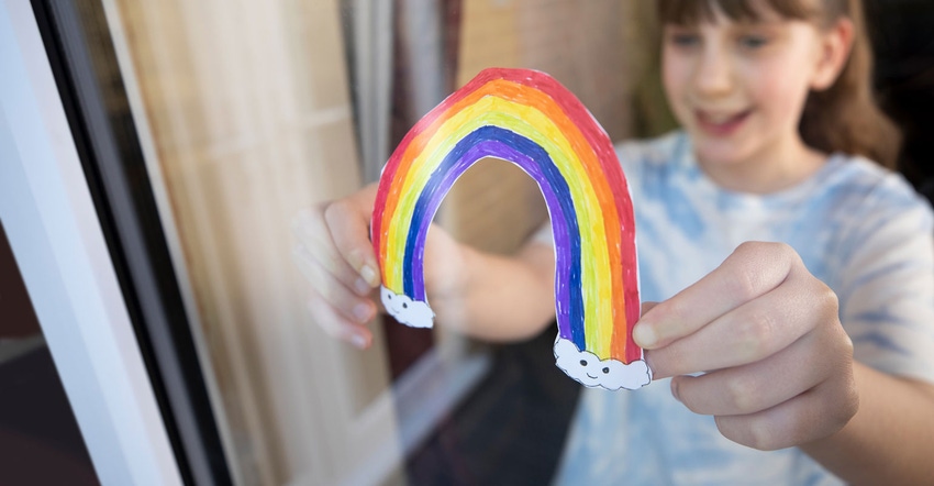 A girl putting picture of a rainbow In window at home during COVID-19 pandemic