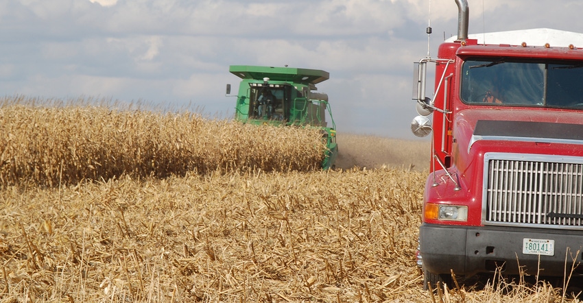 green combine and red truck in field at corn harvesting
