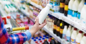 A shopper examines a bottle of milk in the dairy section of the grocery store