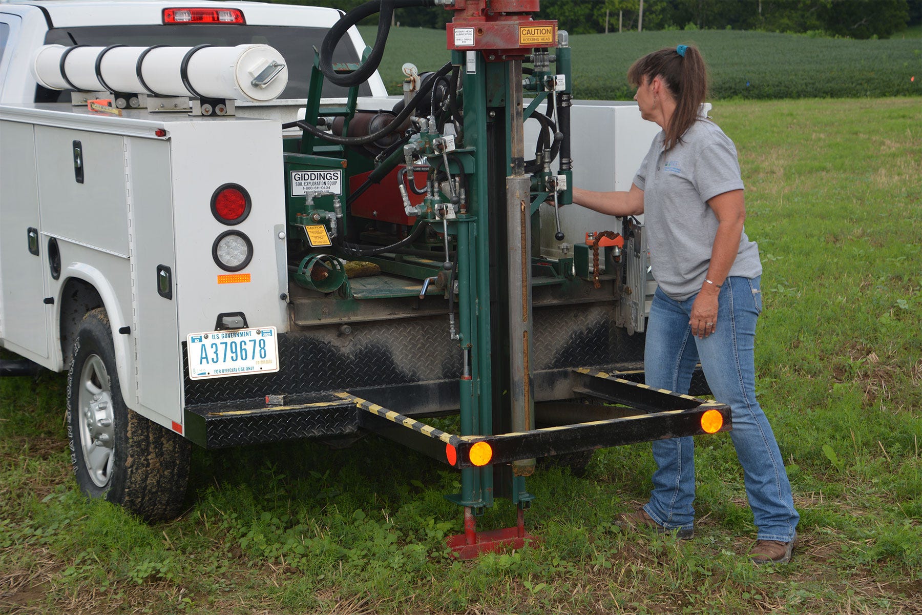 woman stands next to truck with a hydraulic probe for pulling soil sample cores
