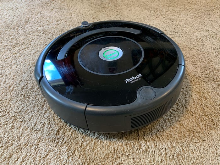 A black circular iRobot, a remote floor vacuum on top of carpet