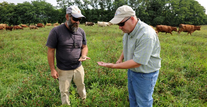 : Local NRCS district agronomist Drew DeLang (right) and farmer Bill Totemeier inspect the clover in a pasture mix of forage 