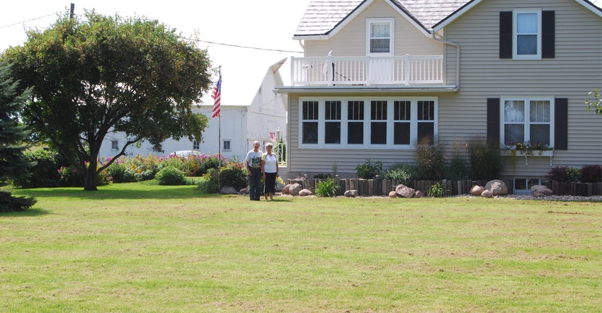 an older couple standing infront of their farmhouse an older couple standing infront of their farmhouse
