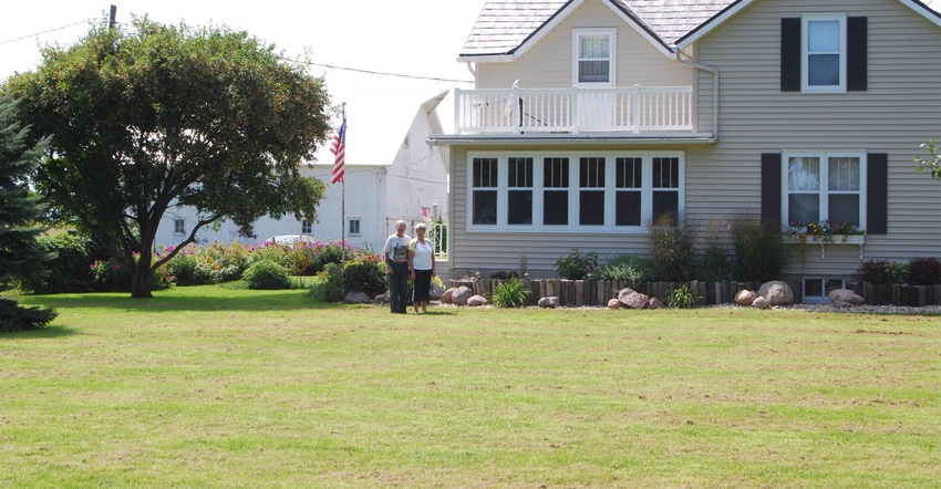 an older couple standing infront of their farmhouse