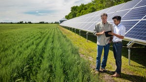 Two farmers review data on a tablet with solar array and field behind them