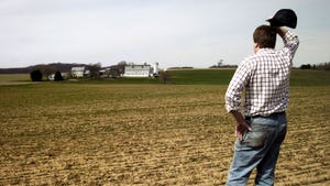 Farmer looking across field at farm operation scratching his head