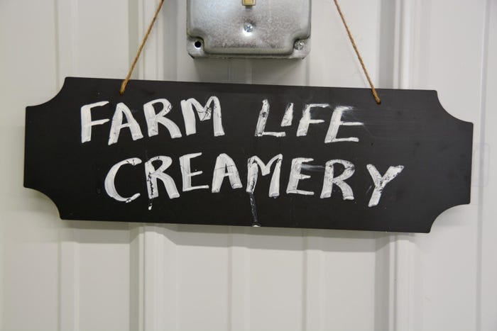 A black sign hanging on a wall with white lettering that reads Farm Life Creamery