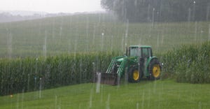 Heavy rain falls on corn crops with tractor parked adjacent to field