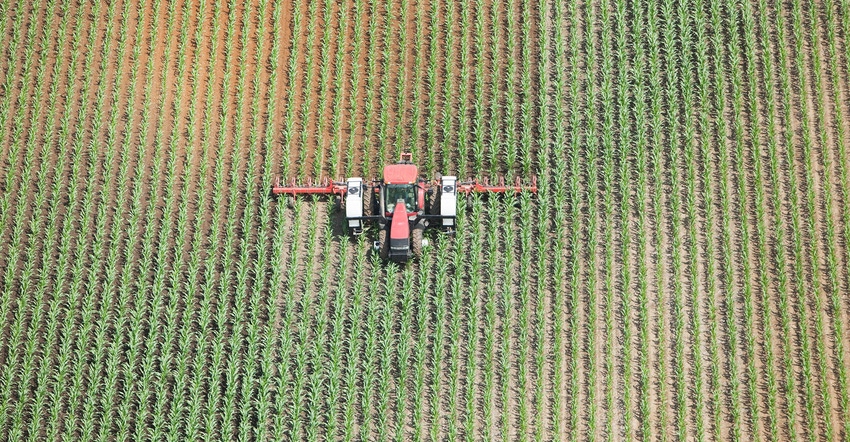 Aerial view of a tractor towing an applicator is spraying liquid nitrogen fertilizer on a late Spring corn field. The left co