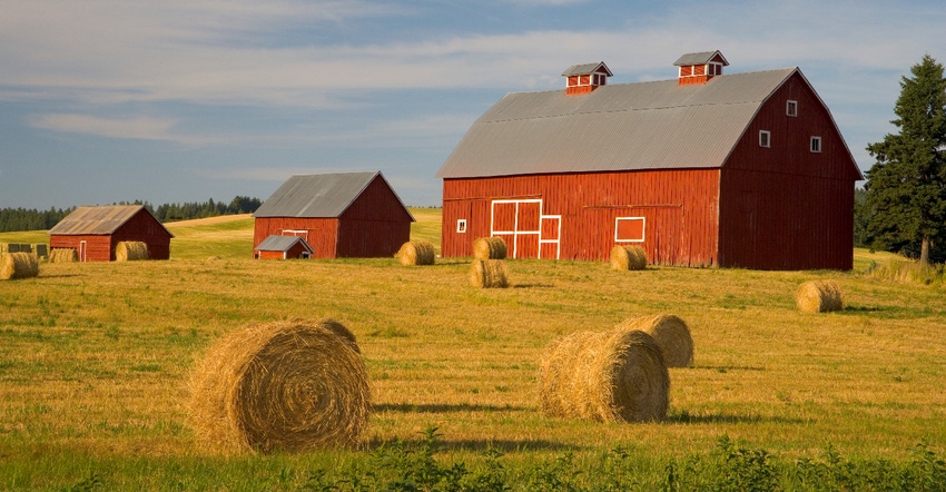 red barn in field surrounded by hay bales