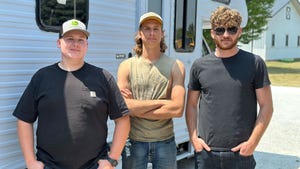 Three young men pose together in front of a trailer