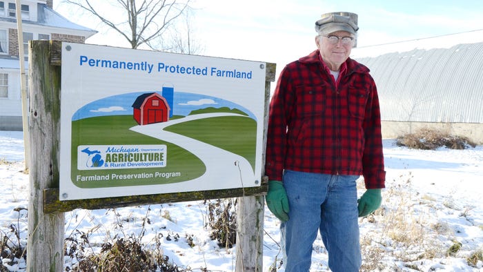 Bob Schultz of Ypsilanti, Michigan smiles next to a permanently protected farmland sign