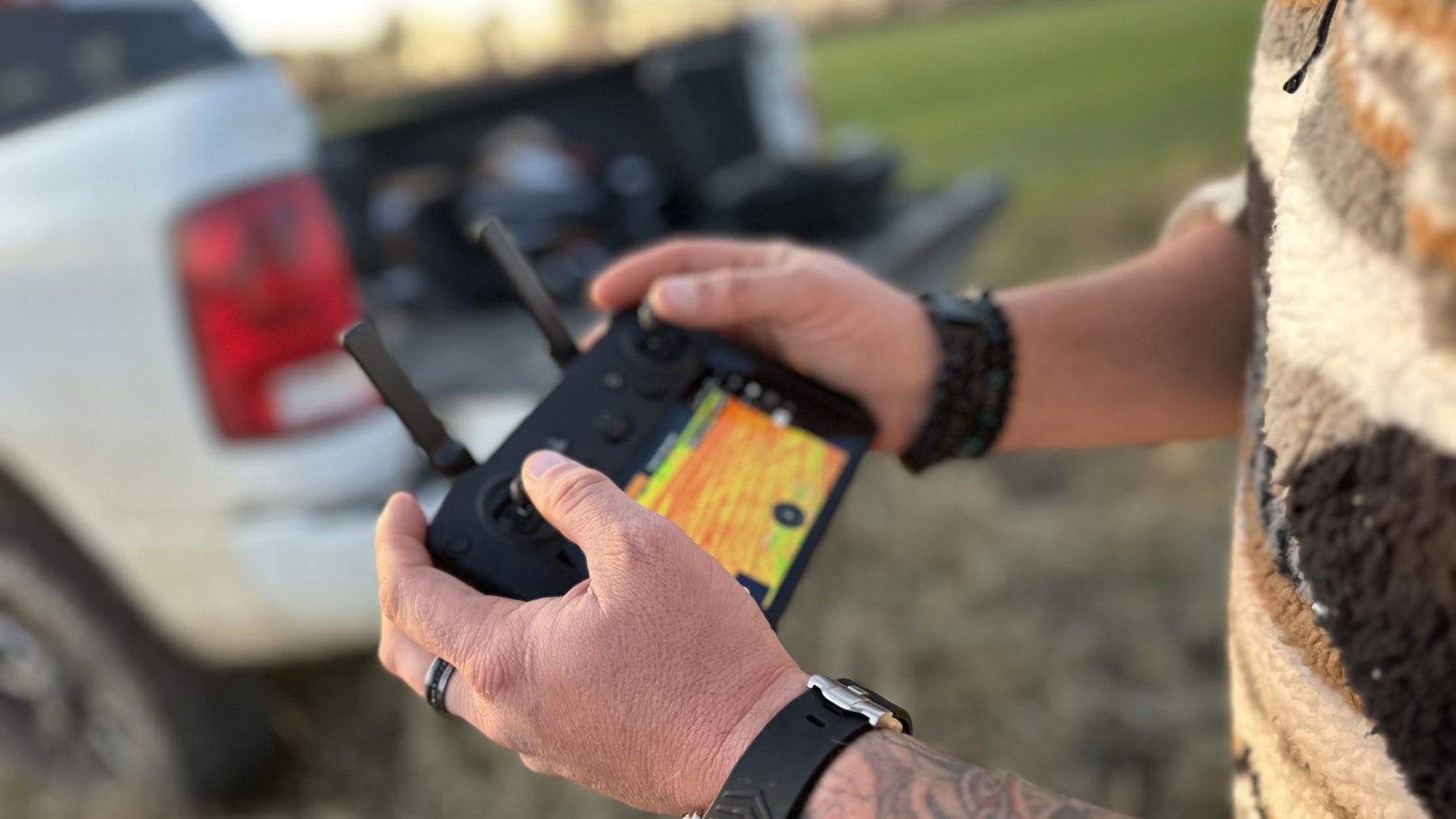 Close up of person holding DJI Mavic Multispectral Drone control, with image of field on screen of control.
