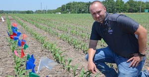 Dan Quinn kneels in young cornfield next to row of flagged plants