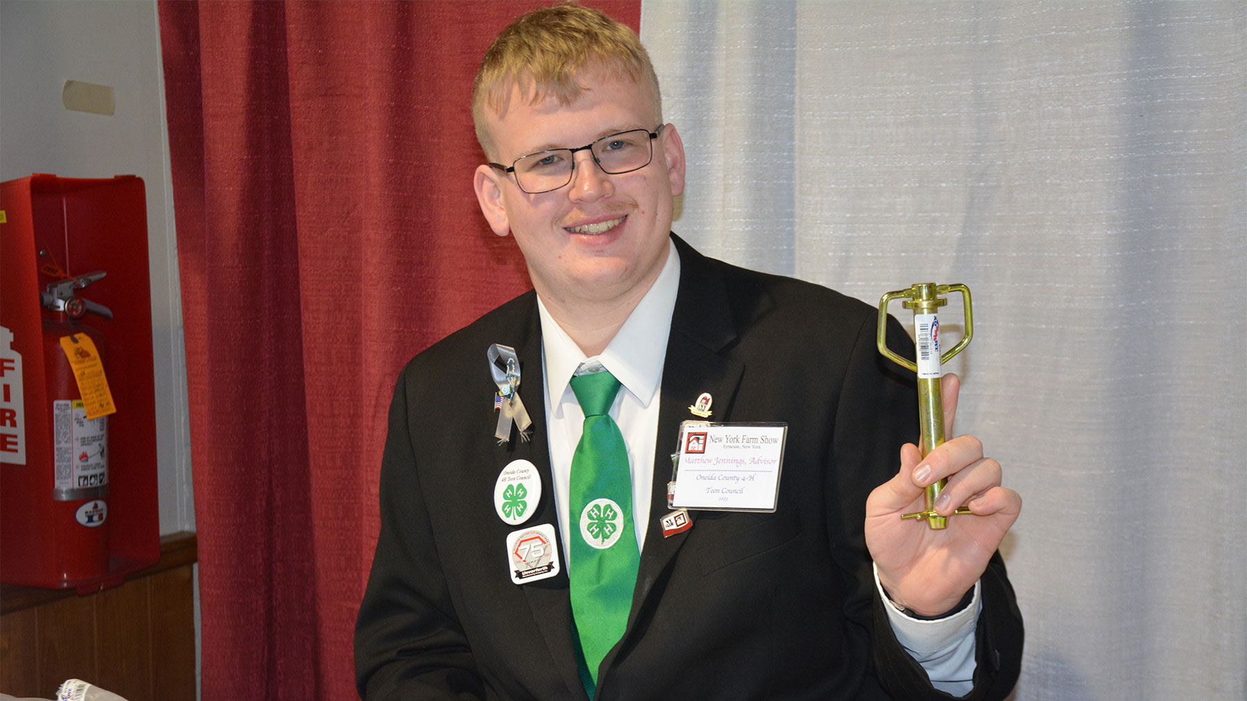 A young man holds up a hitch pin as he smiles