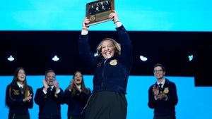 Gracie Murphy holds up a plaque while FFA members cheer behind her