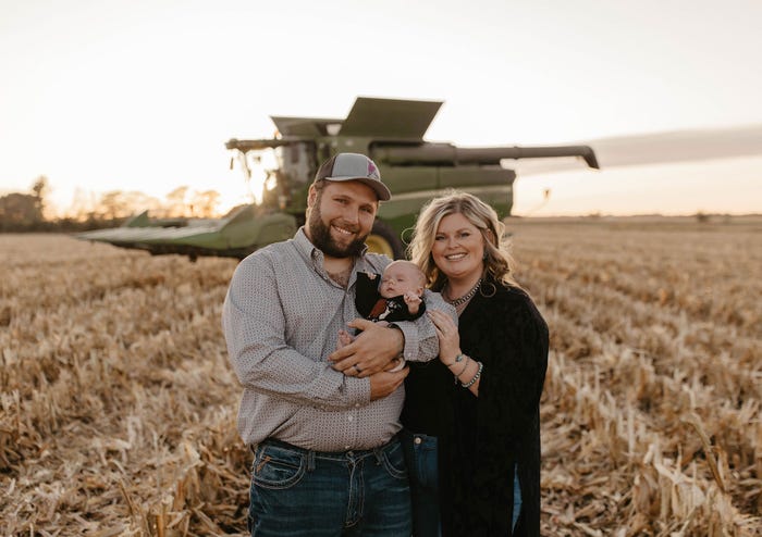 Shelby Lager, his son Hesston and his wife Tannah pose in a field with combine harvester in the background