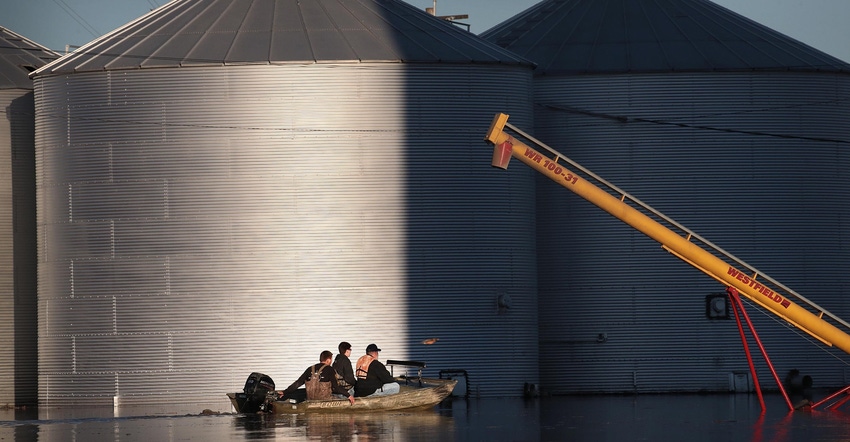 A boat passes by grain bins which are surrounded by floodwater