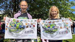Two girls each holding a towel decorated with Odyssey of the Mind pin collection.