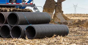 Black corrugated water drainage pipe, field tile, in farm field with tile plow or ditcher in background