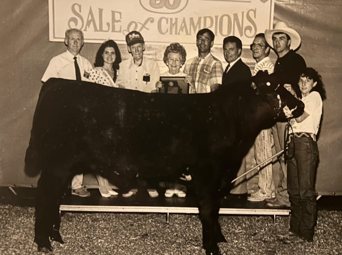 young girl poses at halter of steer with group of people behind them
