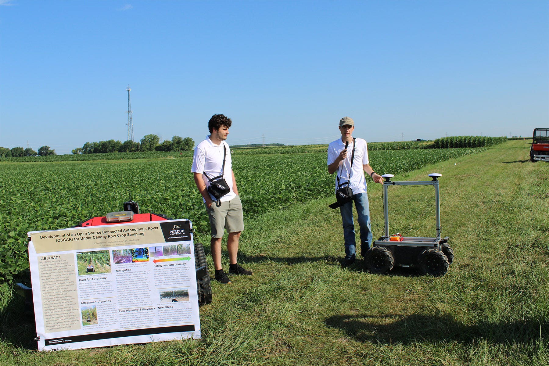 2 college students give a presentation with a robot in front of a soybean field 2 college students give a presentation with a robot in front of a soybean field