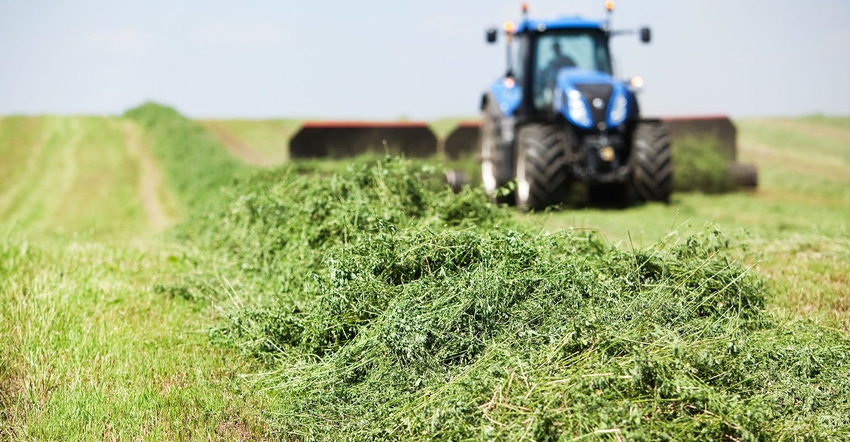 A tractor is towing a merger on a cut alfalfa (hay) field.