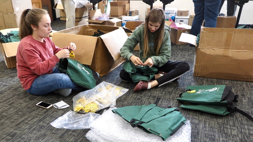 2 teenage girls sitting on floor amid cardboard boxes and green cloth bags