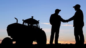 Two farmers shaking hands with tractor in the background