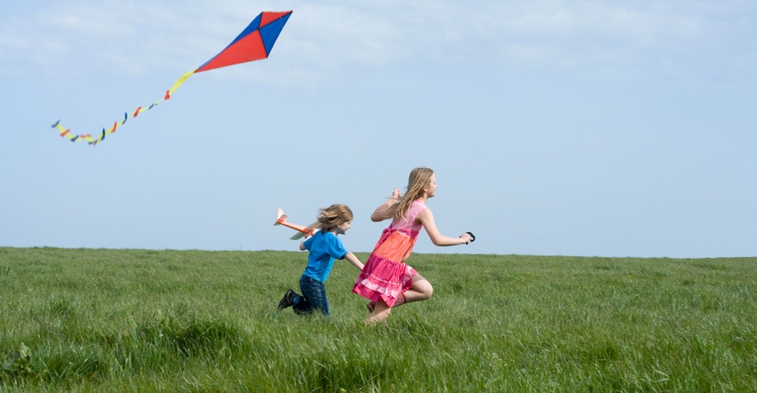 Boy holding small airplane and girl running through field with kite in air Boy holding small airplane and girl running through field with kite in air
