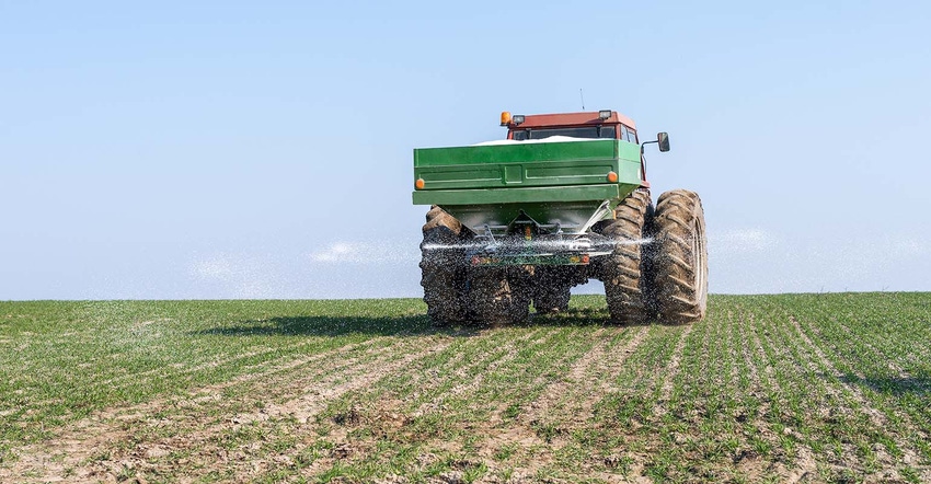 Tractor and wagon spreading fertilizer on young wheat